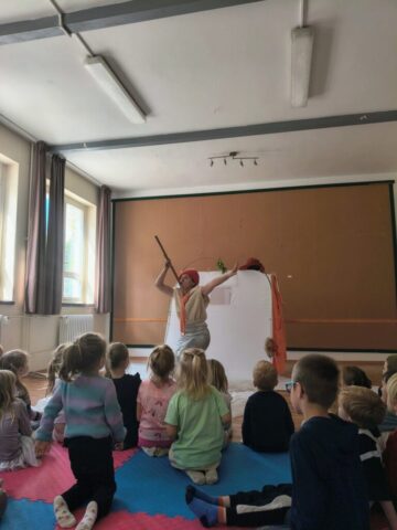 Buergerhaus-Bornim-VergissMeinFuchs-2026-3 Jana Kühn spielt mit ausgebreiteten Armen vor dem Zelt, die Kinder schauen zu